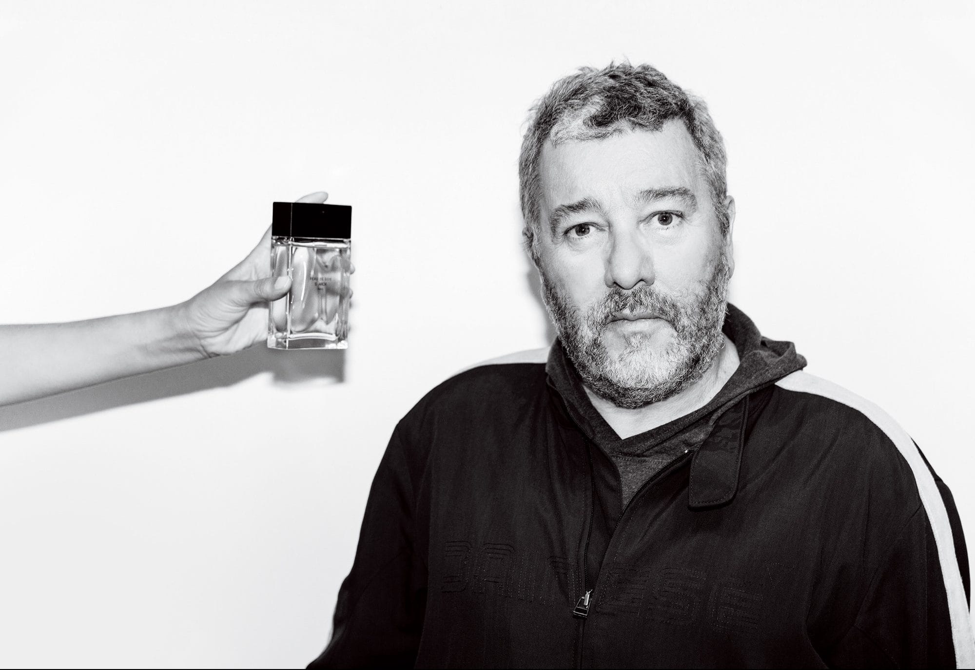 Black and white photo of a man with short hair next to a hand holding a perfume bottle