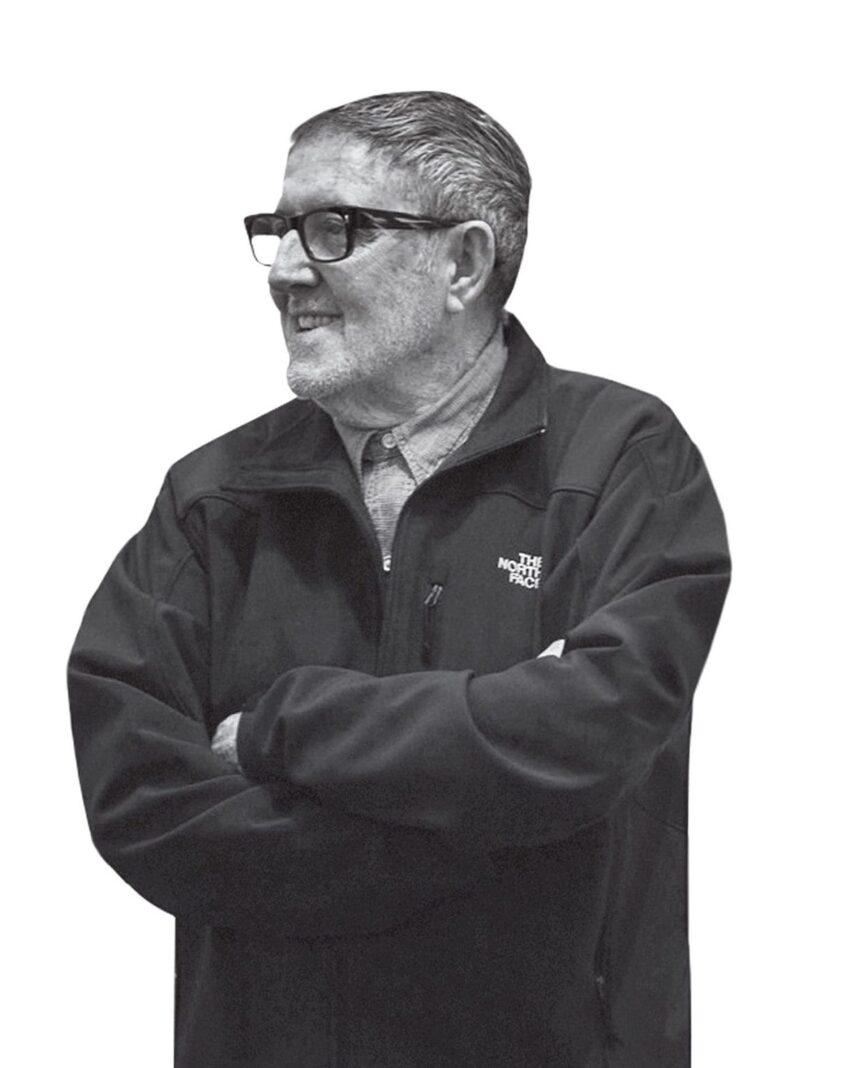 Man in glasses and a North Face jacket, smiling and looking to the side with arms crossed.