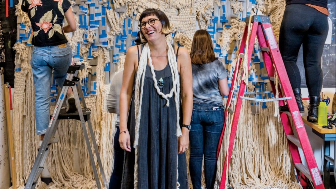 Group of people working on a large macramé project with ropes and ladders in a creative studio setting.