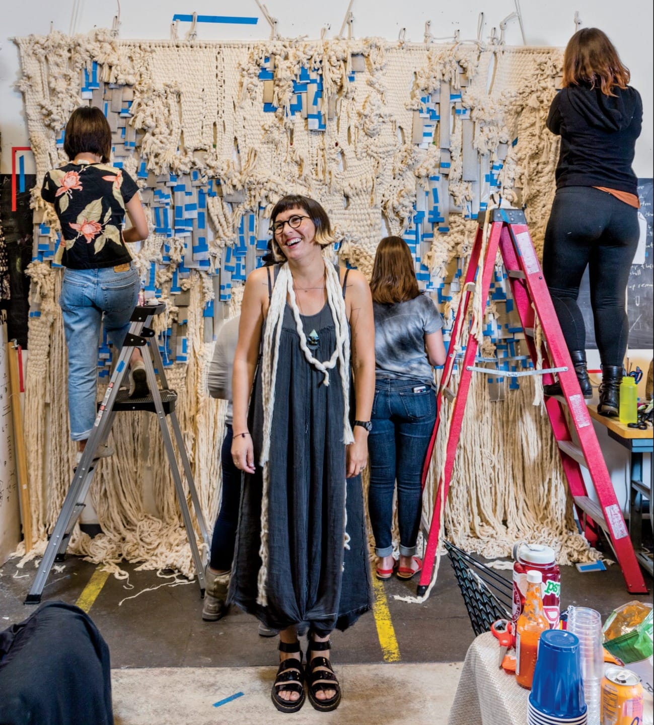 Group of people working on a large macramé project with ropes and ladders in a creative studio setting.