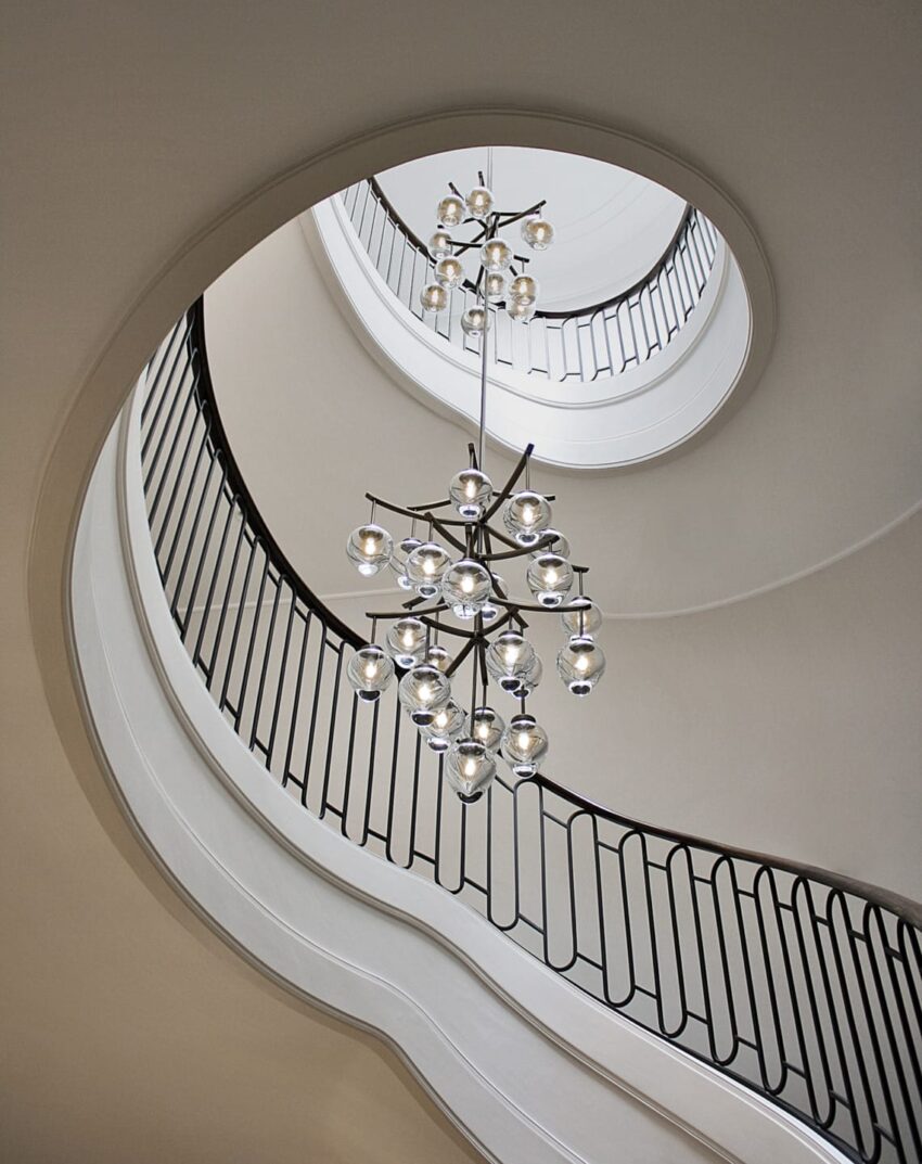 Spiral staircase with an elegant, modern chandelier hanging in the center, surrounded by smooth, curved railings.