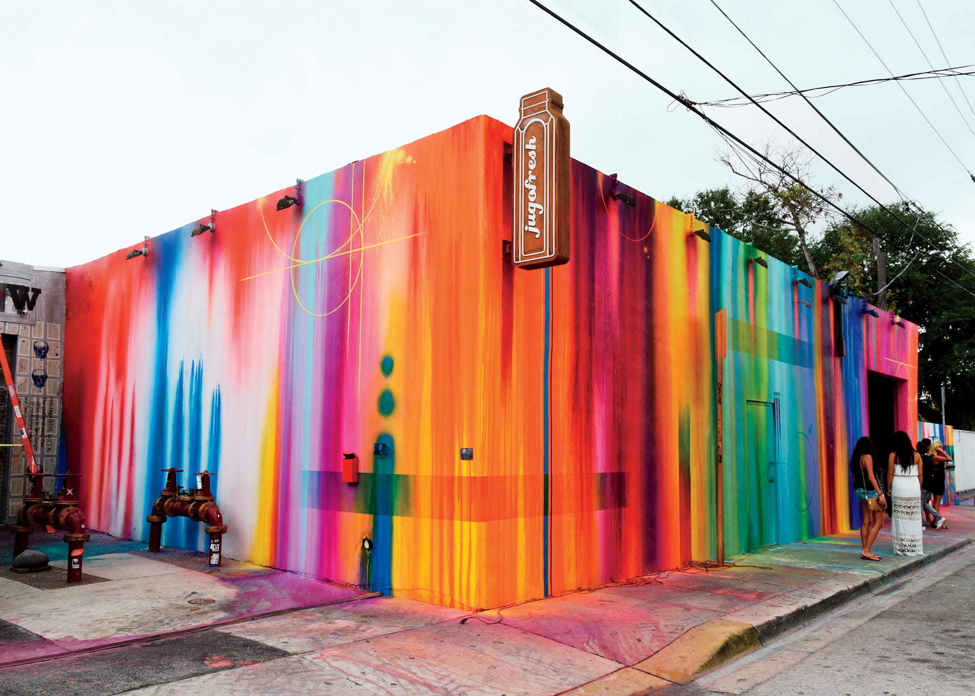 Colorful building with vibrant, multicolored mural and street sign, located on a city street with a few people walking by.