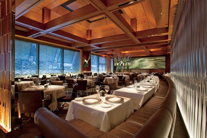 Elegant restaurant interior with wooden ceiling, neatly set tables, and large scenic wall art.