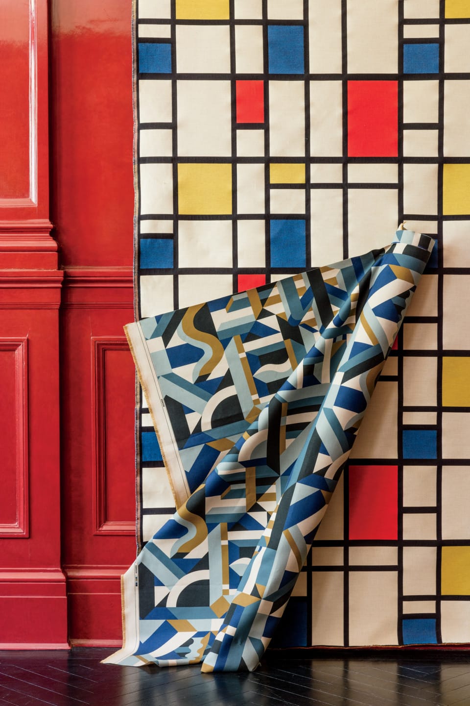 Geometric patterned wallpaper with red, yellow, and blue squares and a rolled section revealing a different design.