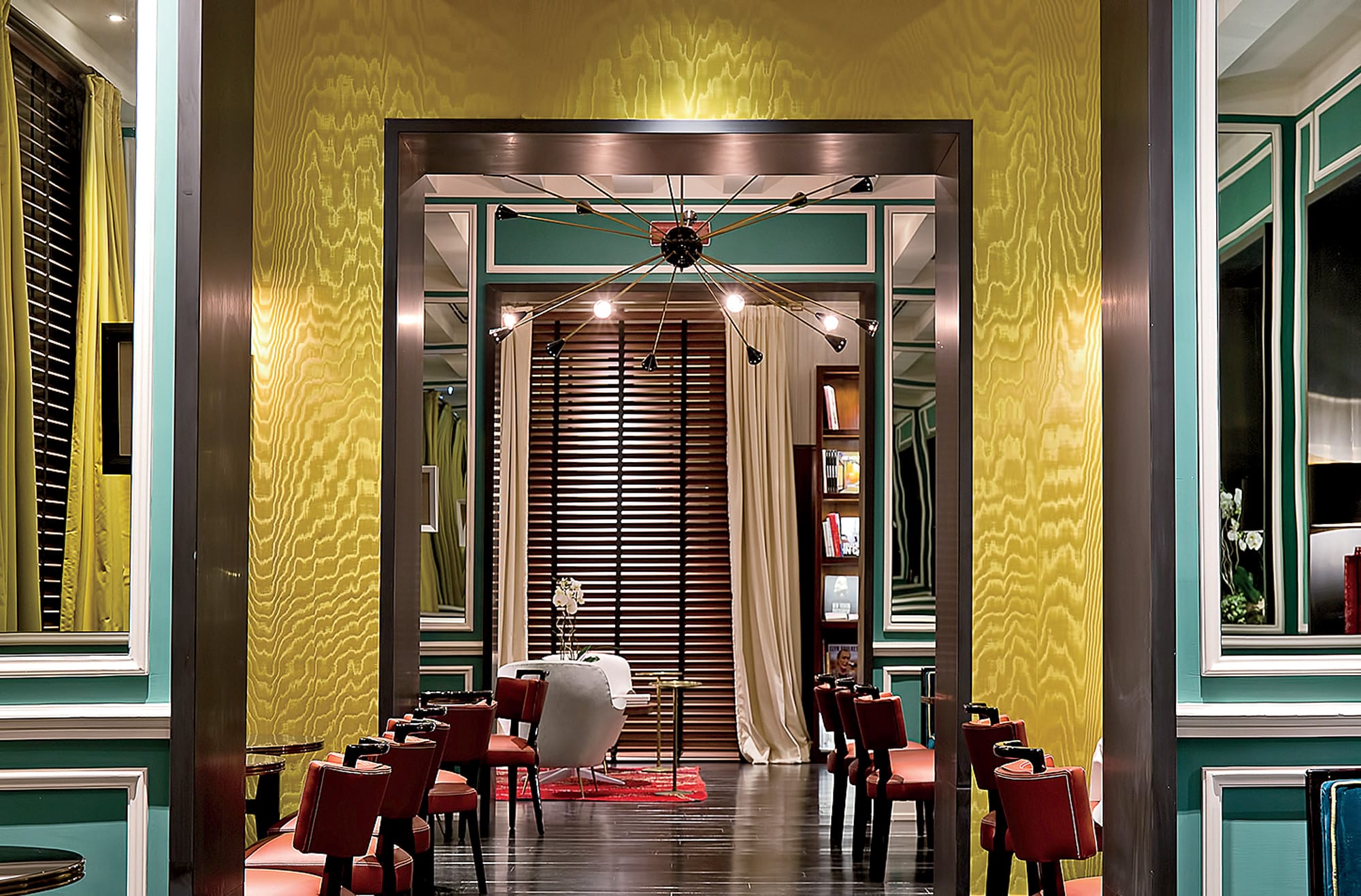 Modern interior of a stylish restaurant with elegant decor, red chairs, a central light fixture, and wooden accents.