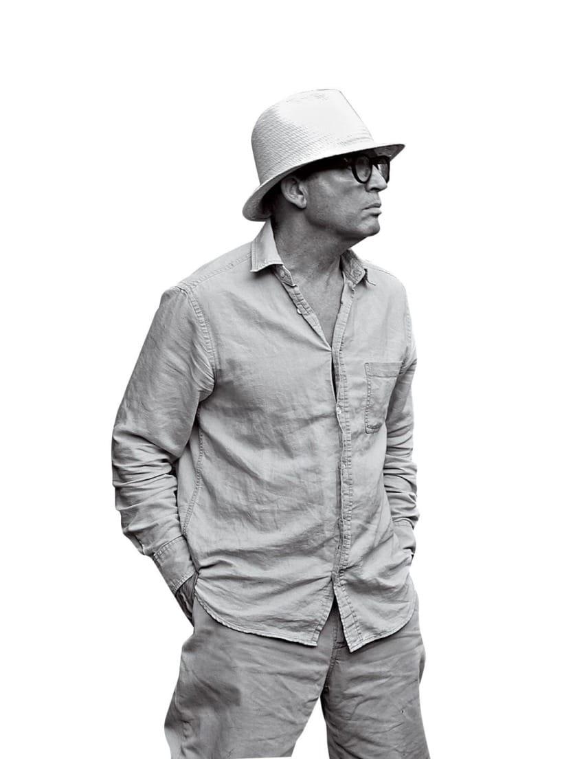 Man in a hat and glasses wearing a casual outfit, looking to the side with hands in pockets.
