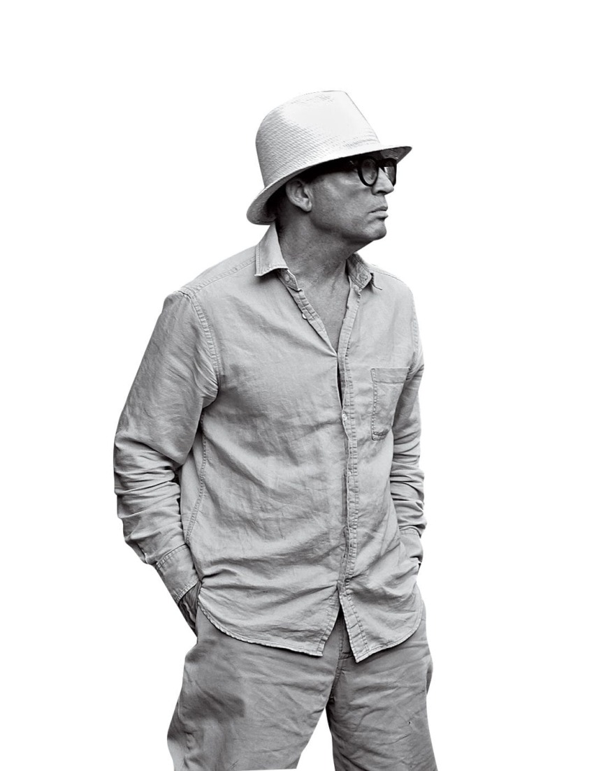 Man in a hat and glasses wearing a casual outfit, looking to the side with hands in pockets.