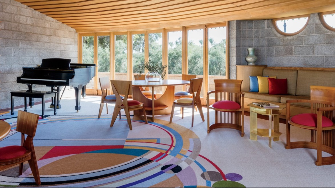 Spacious living room with modern furniture, vibrant circular rug, grand piano, and large windows offering natural light