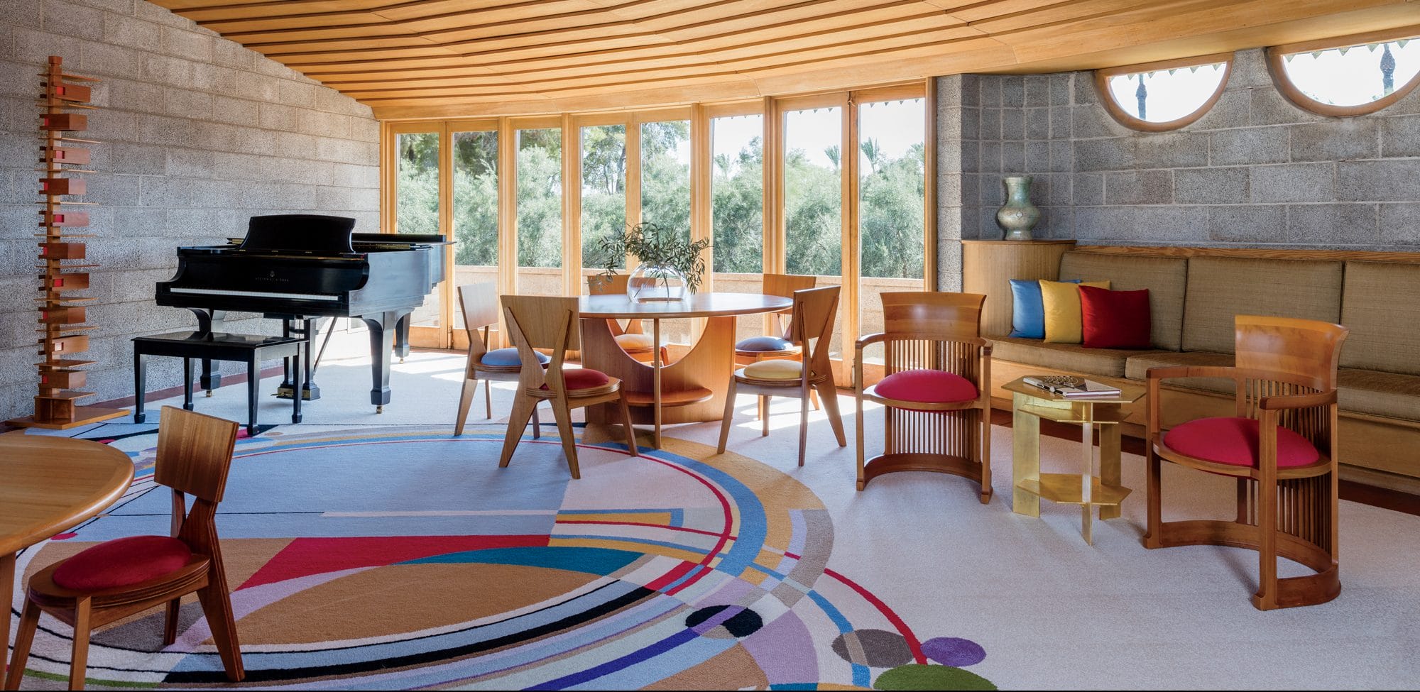 Spacious living room with modern furniture, vibrant circular rug, grand piano, and large windows offering natural light