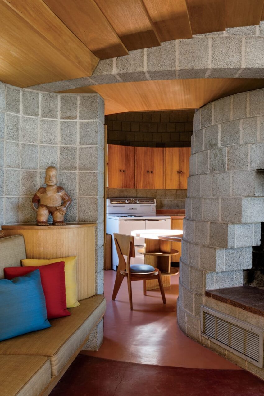 Cozy interior with curved stone walls, wooden ceiling, colorful cushions, and rustic decor in a small dining area.
