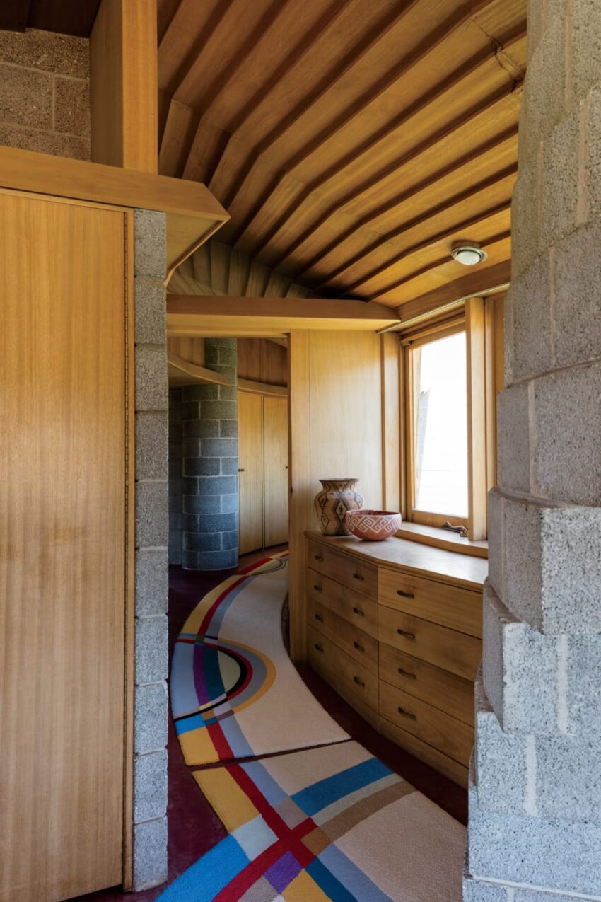 Curved hallway with wooden ceiling, colorful carpet, concrete walls, and built-in wooden drawers in modern architecture.