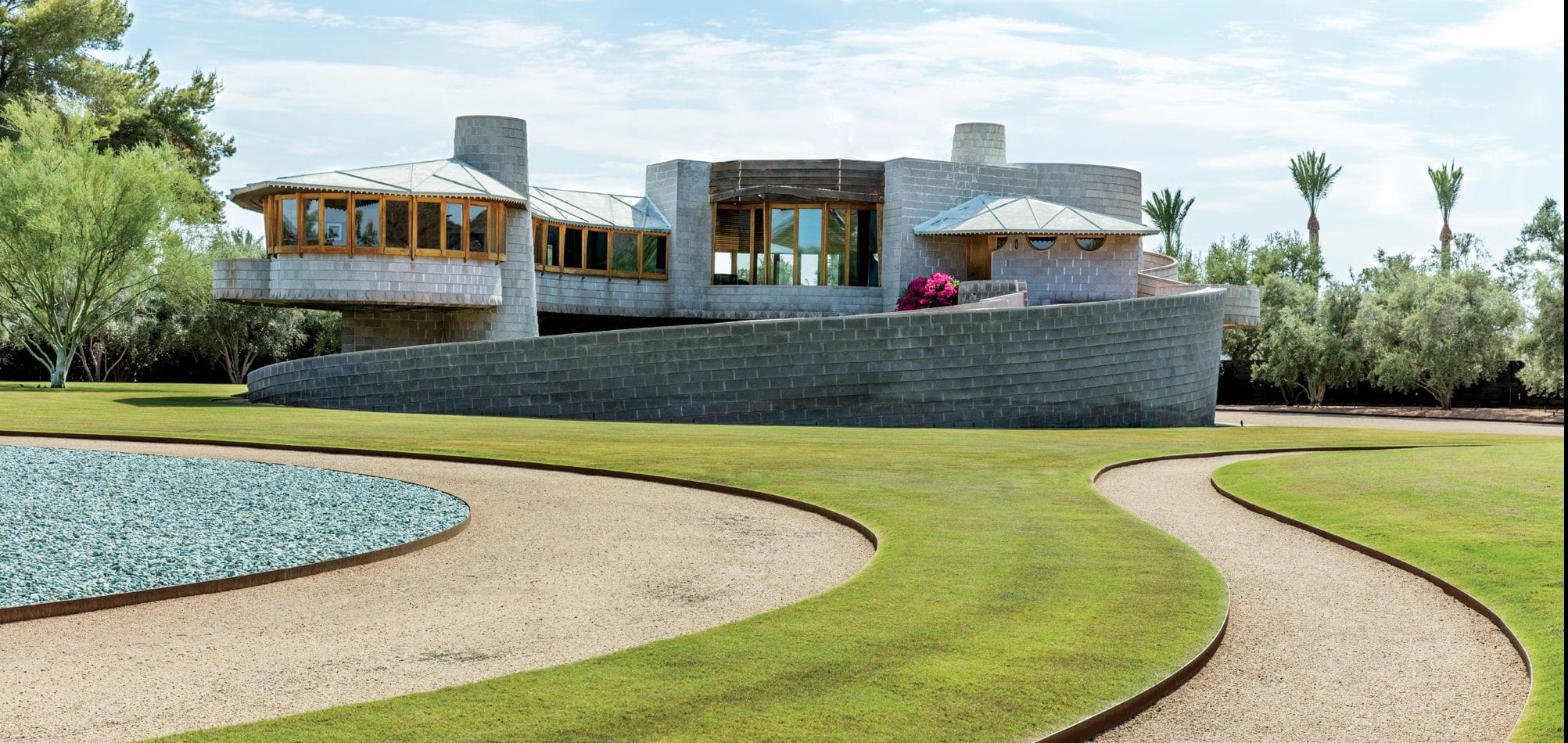 Modern architectural building with circular design, surrounded by landscaped lawns and pathways under a blue sky.