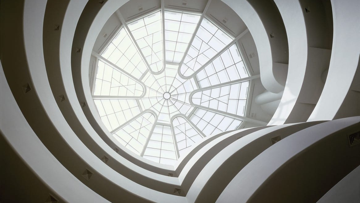 View of a spiral staircase looking up through a glass ceiling with a modern architectural design.