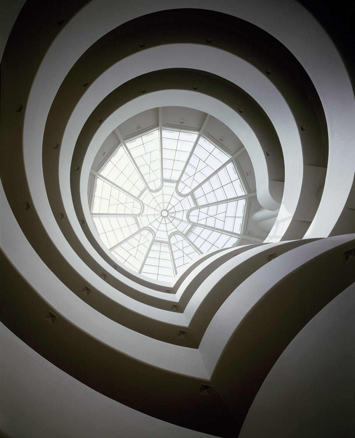View of a spiral staircase looking up through a glass ceiling with a modern architectural design.
