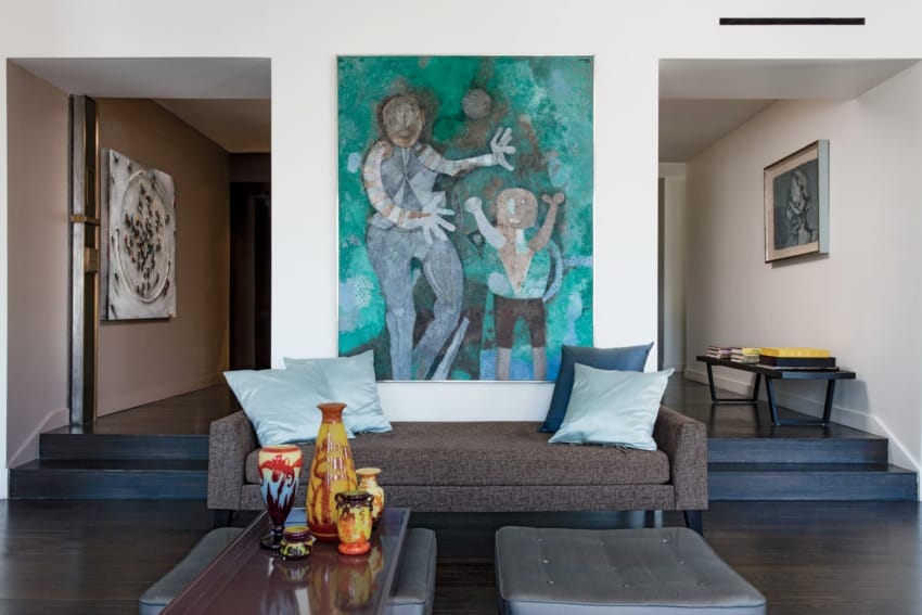 Modern living room with large abstract painting, gray sofa, colorful vases on table, light blue cushions, and art on walls.