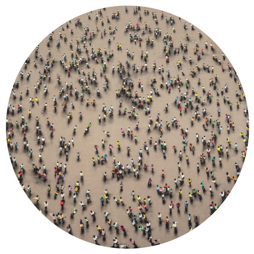 Aerial view of a large group of people walking in various directions on an open space with colorful clothing.