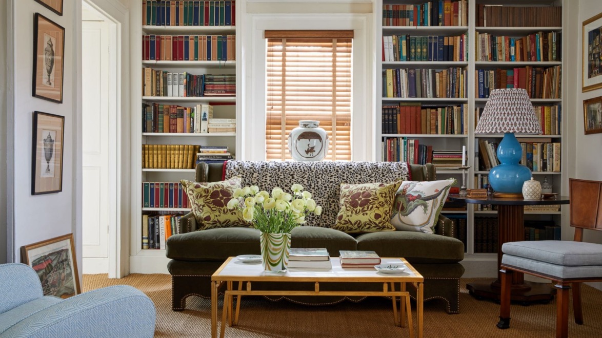 Cozy living room with a green sofa, bookshelves, a coffee table with flowers, and a decorative lamp.