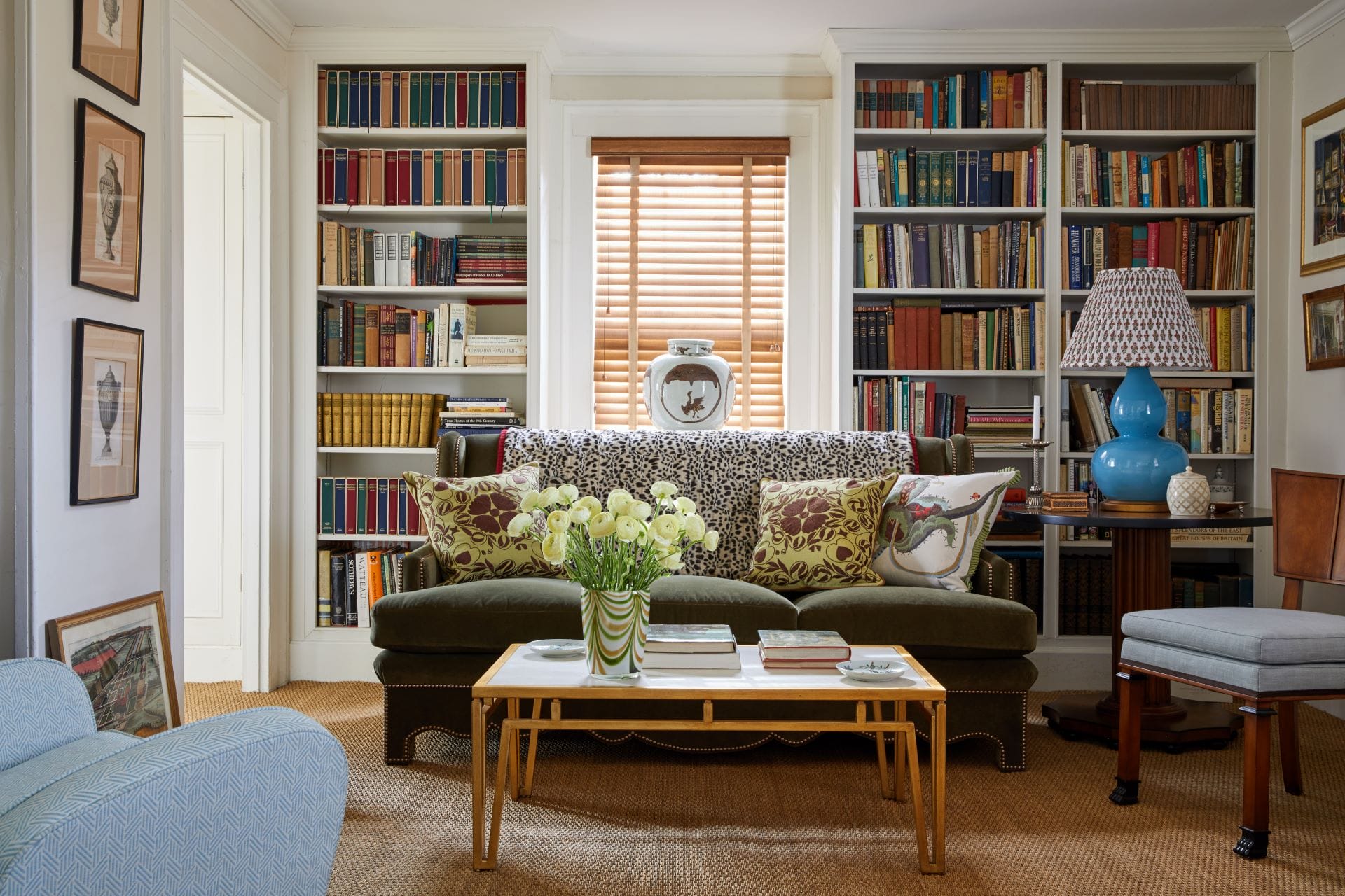 Cozy living room with a green sofa, bookshelves, a coffee table with flowers, and a decorative lamp.