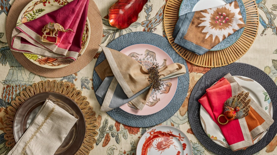 Elegant table setting with decorative plates, colorful napkins, and unique napkin rings on a patterned tablecloth.