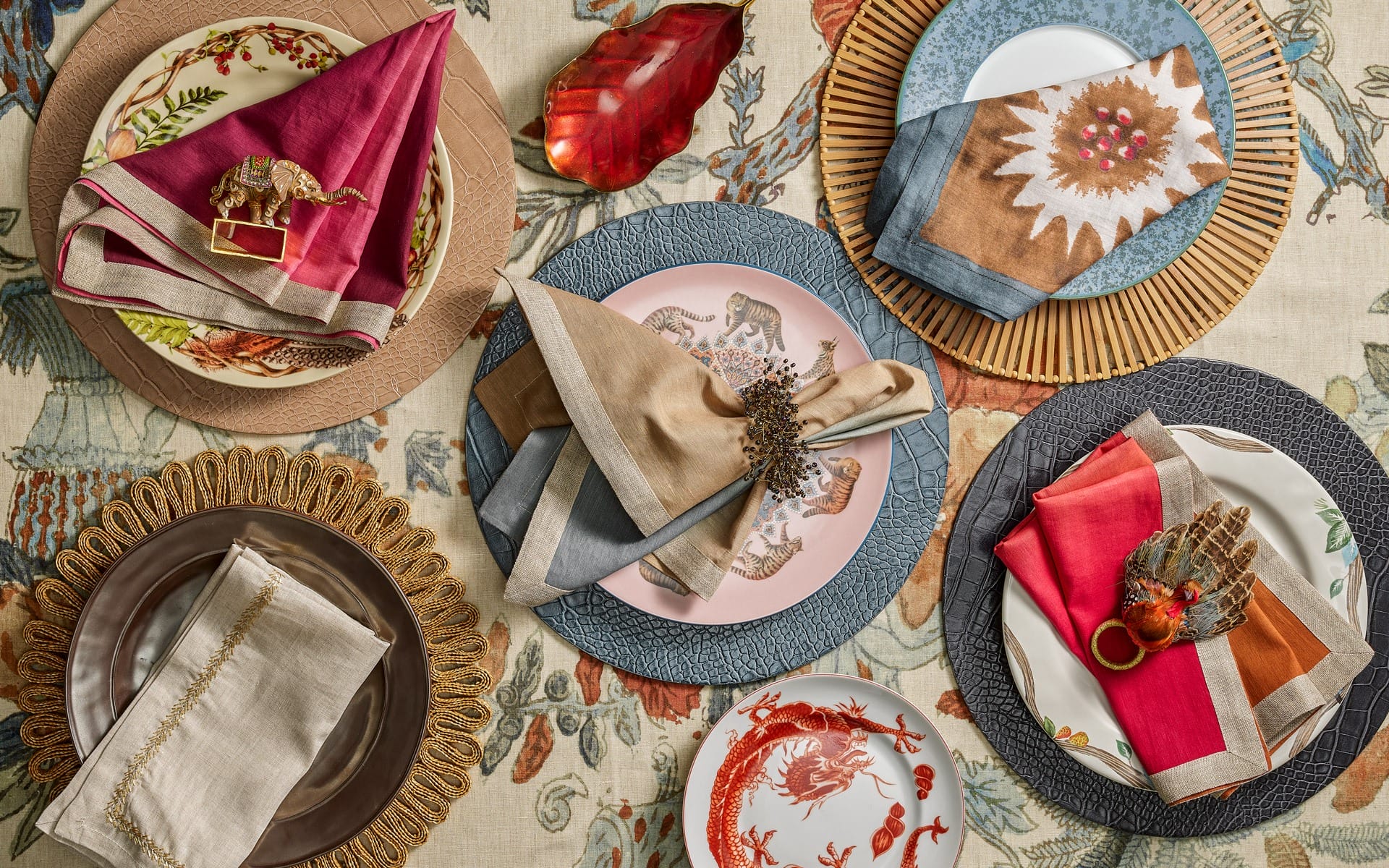 Elegant table setting with decorative plates, colorful napkins, and unique napkin rings on a patterned tablecloth.
