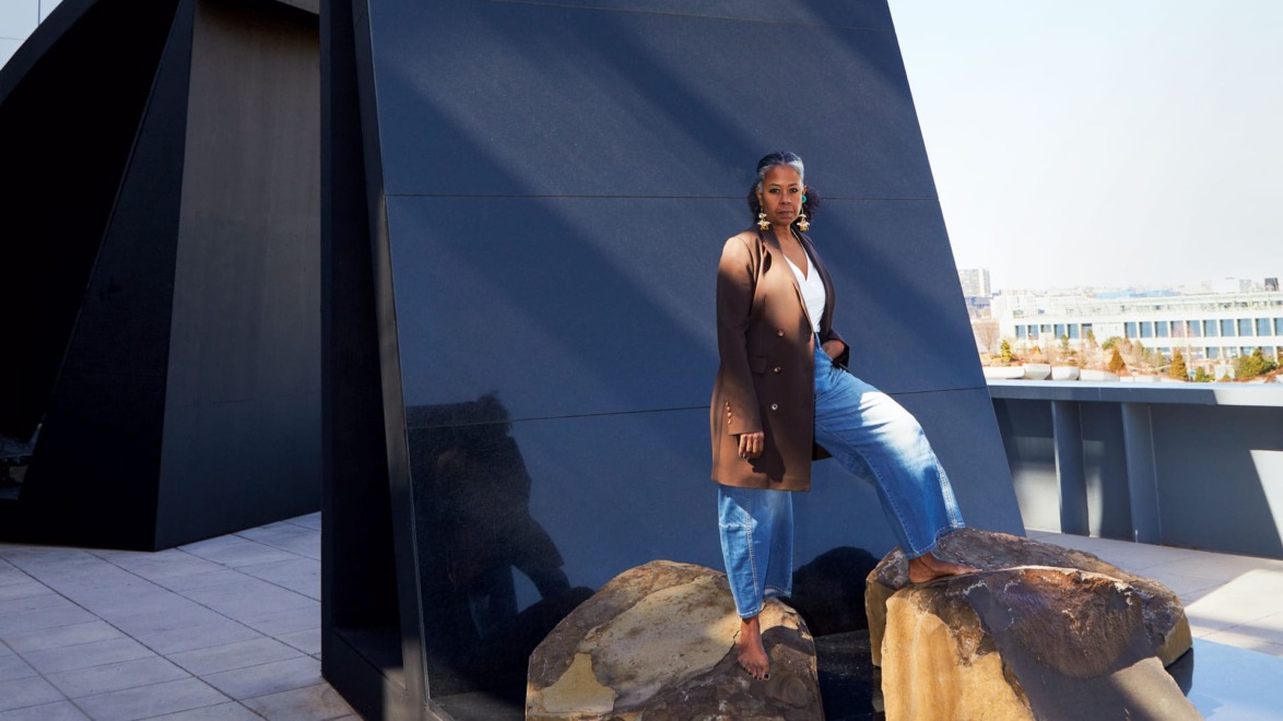 Person standing confidently on rocks in front of a modern black architectural structure on a sunny day.