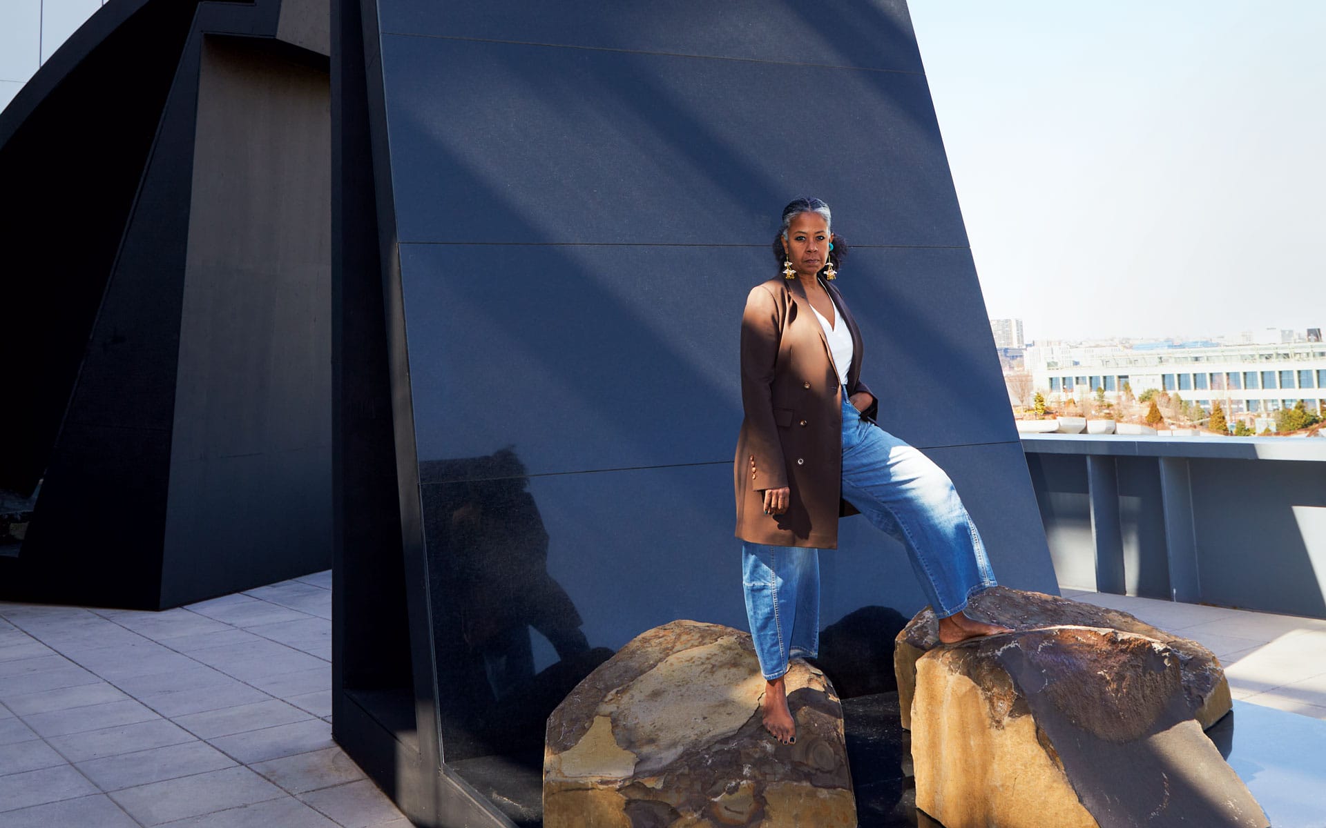 Person standing confidently on rocks in front of a modern black architectural structure on a sunny day.
