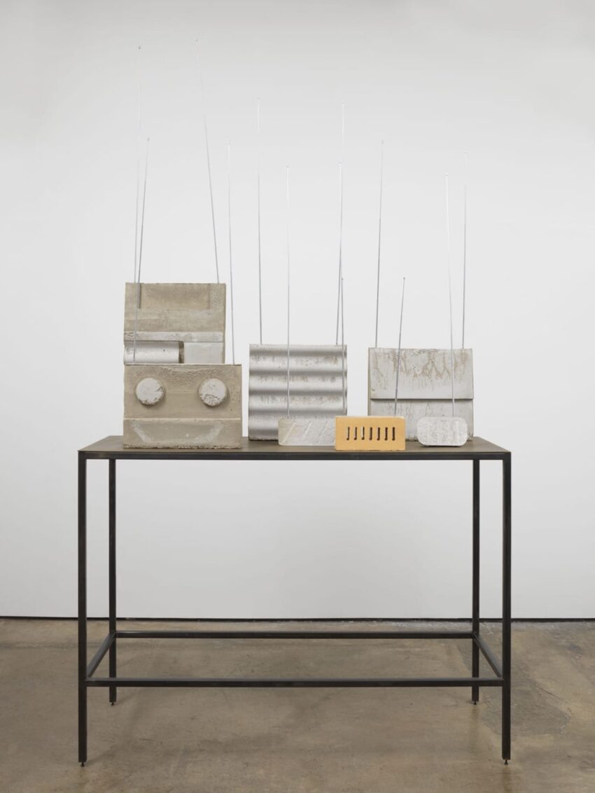 Five abstract sculptures resembling radios on a black metal table against a plain white background.