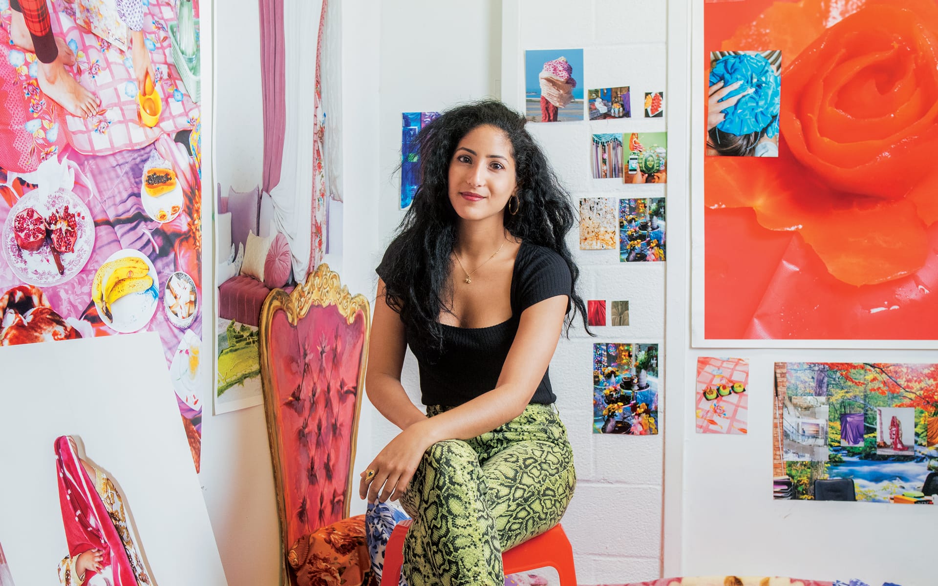 Person sitting in a colorful art studio surrounded by vibrant and abstract paintings on the walls.