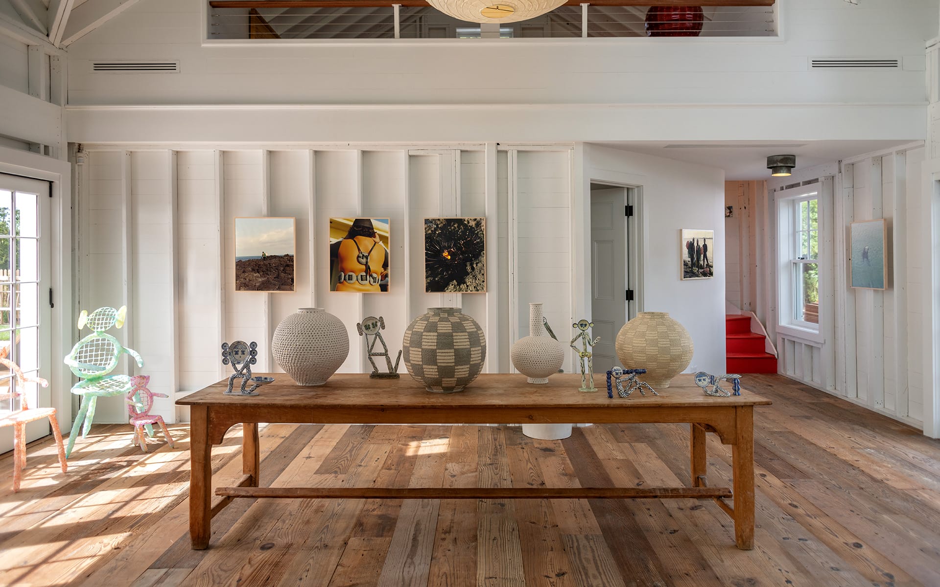 Sunny art gallery with wooden floor, showcasing sculptures and framed artworks on white walls with natural light.