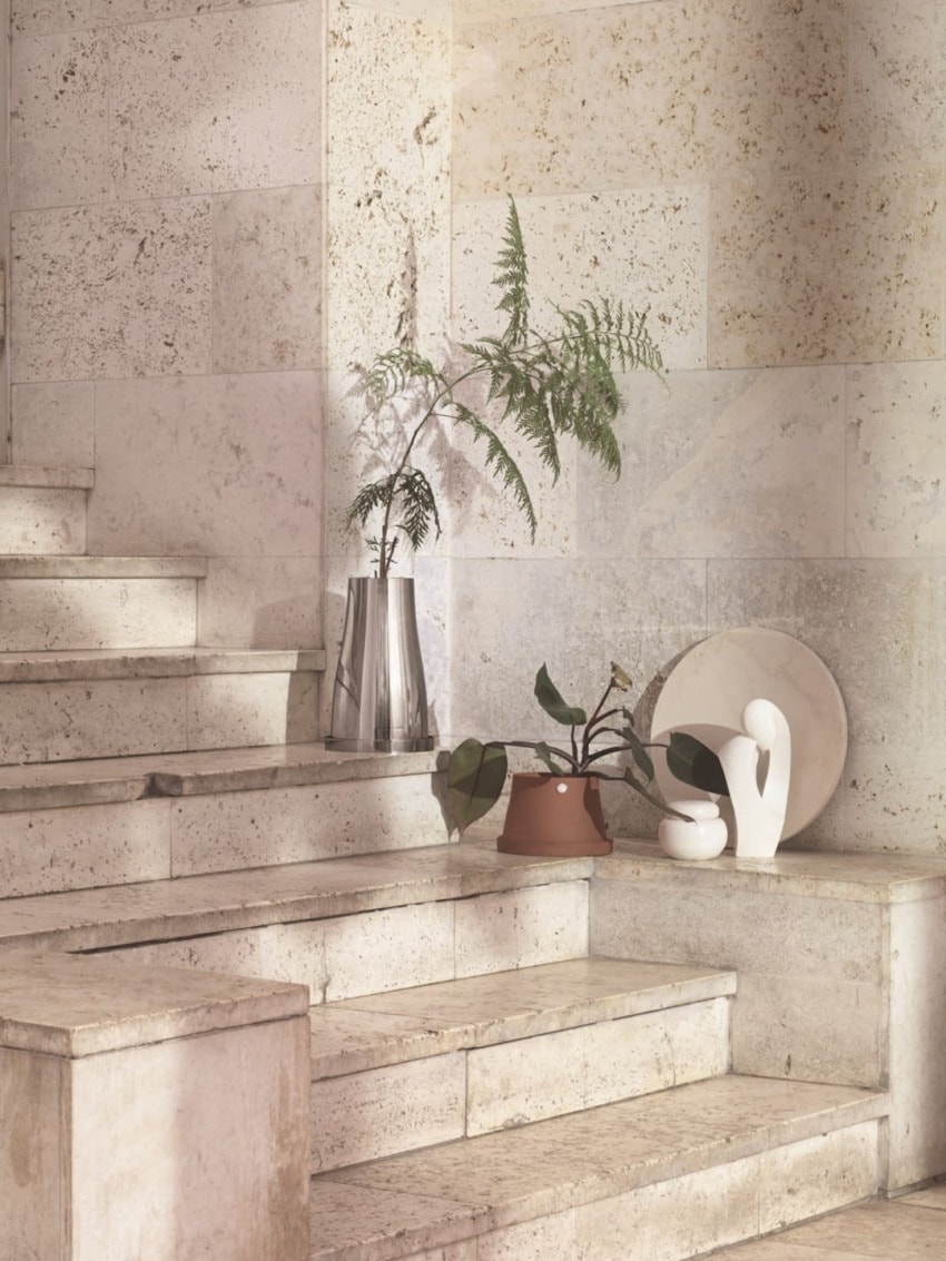 Minimalist stone staircase with decorative plants on steps, including a sculpture and a vase, against a textured wall.