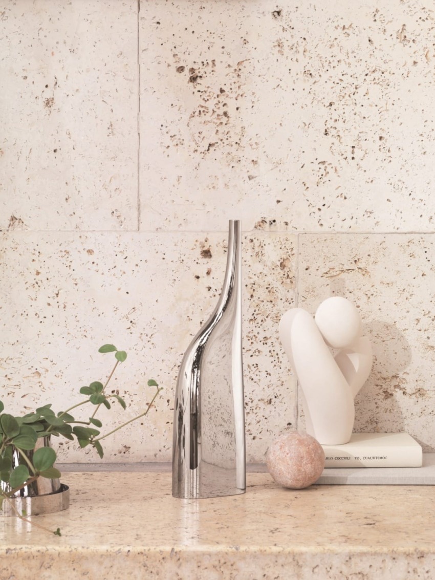 Elegant modern vase and abstract sculpture on a stone shelf with plants, creating a minimalist aesthetic.