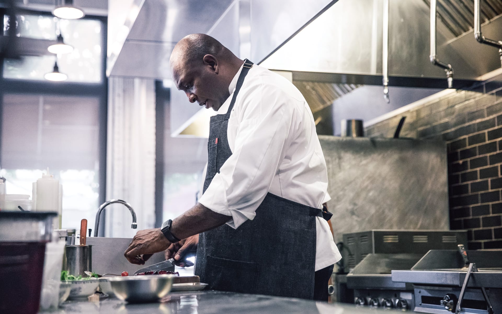 Chef preparing food in a commercial kitchen while wearing a white shirt and gray apron.