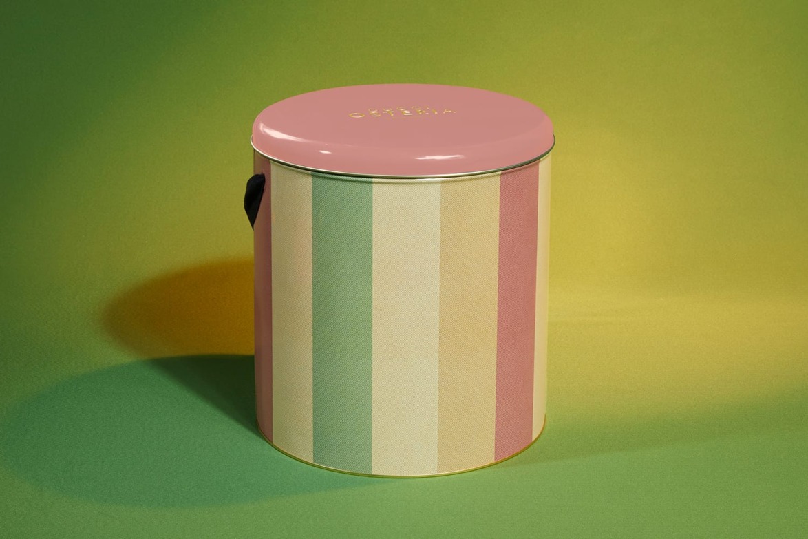 Colorful striped cylindrical tin with a pink lid set against a green background.