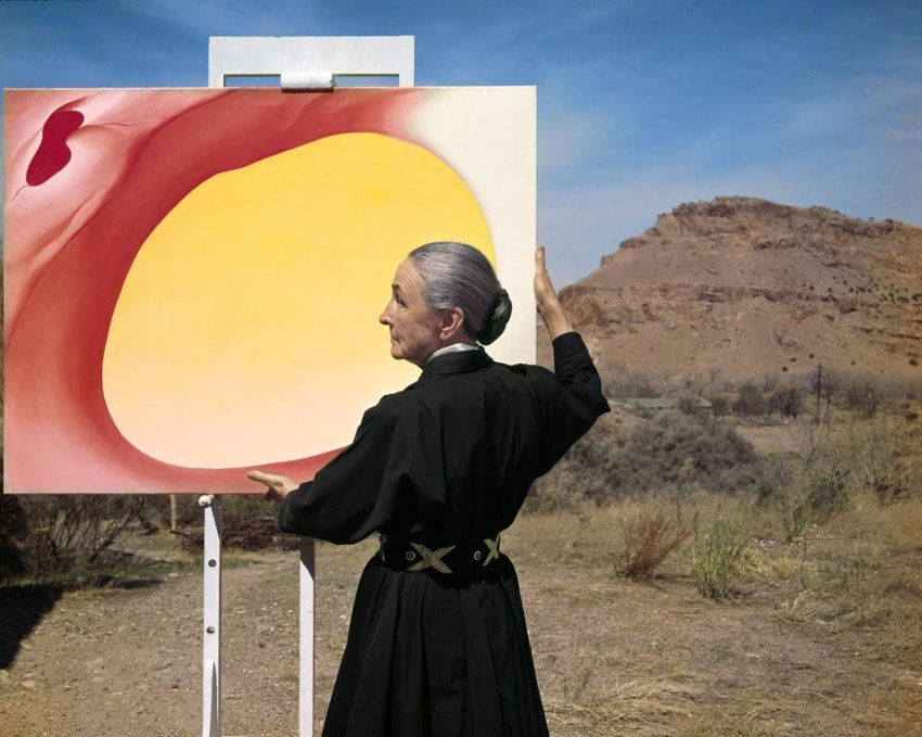 Artist painting a large abstract canvas outdoors with a desert landscape in the background.