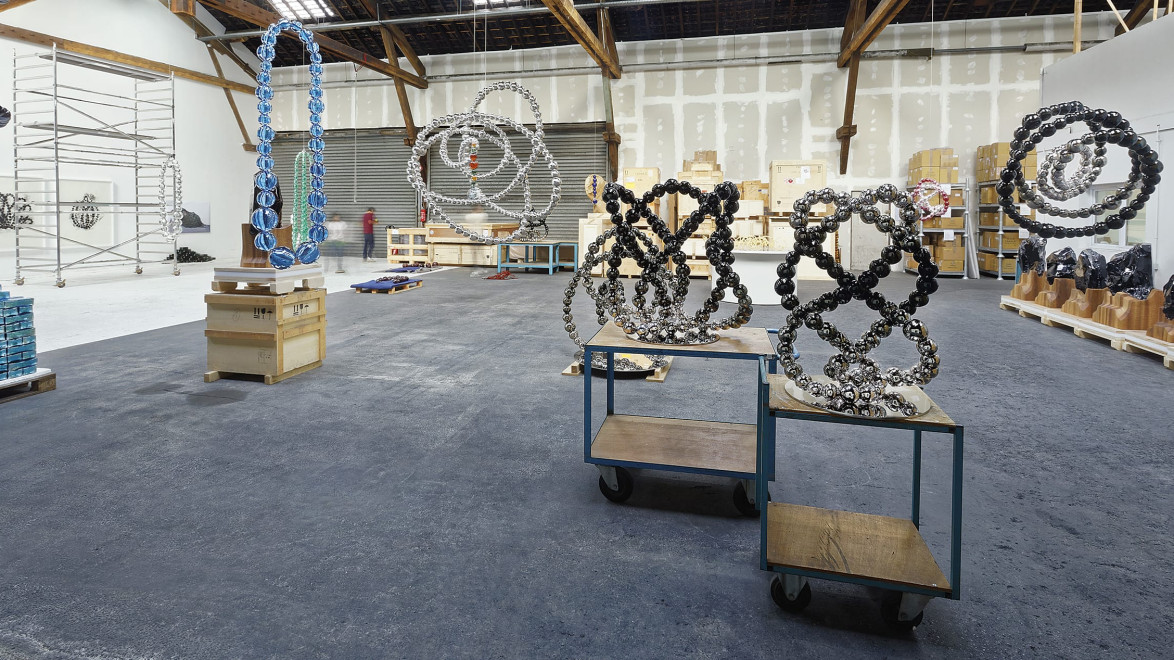 Art installation in a spacious warehouse with large abstract sculptures and wooden beams in the background.
