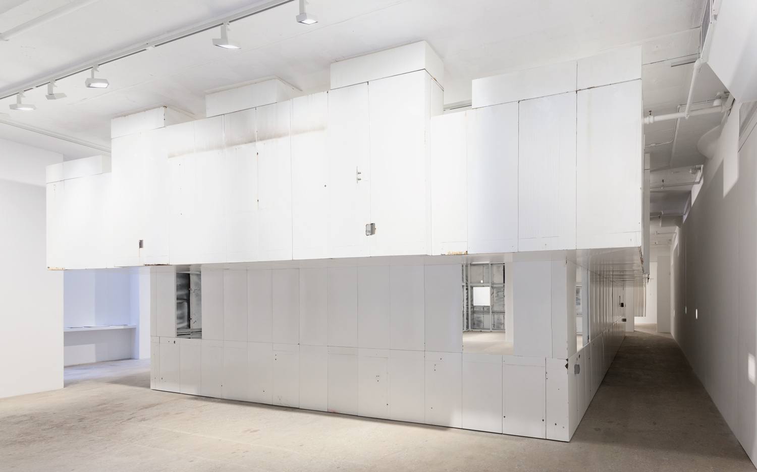 Modern white minimalist interior space with geometric architectural design and ceiling lights.