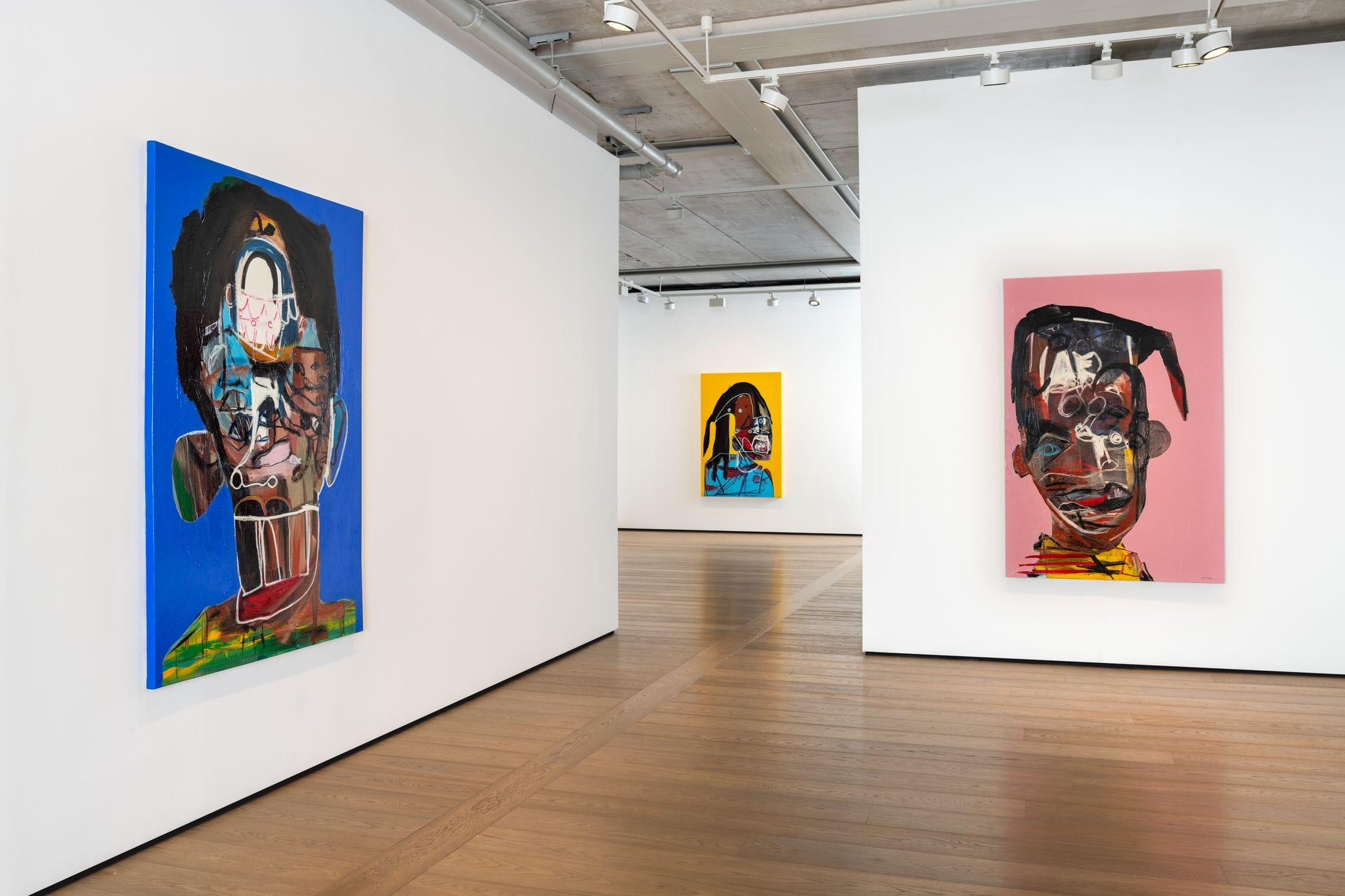 Art gallery interior with three vibrant, abstract paintings on white walls, featuring colorful, expressive human faces.