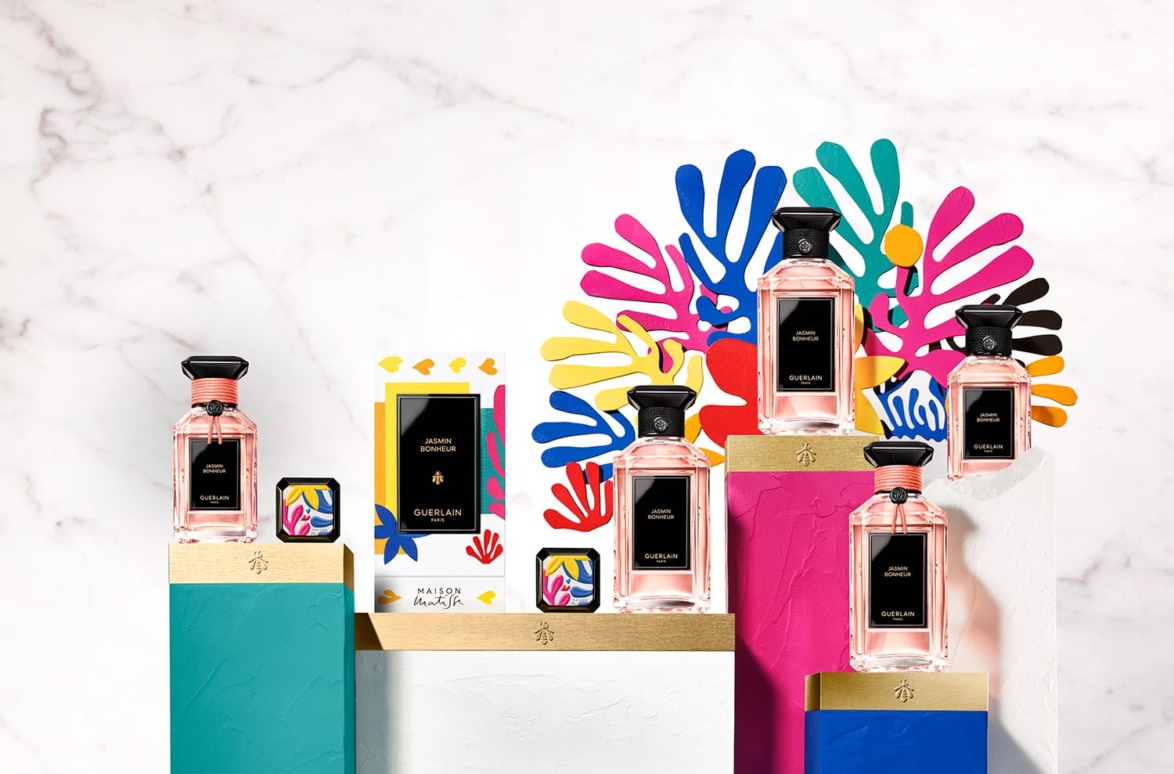 Colorful display of perfume bottles on geometric stands with vibrant abstract floral decorations in the background.