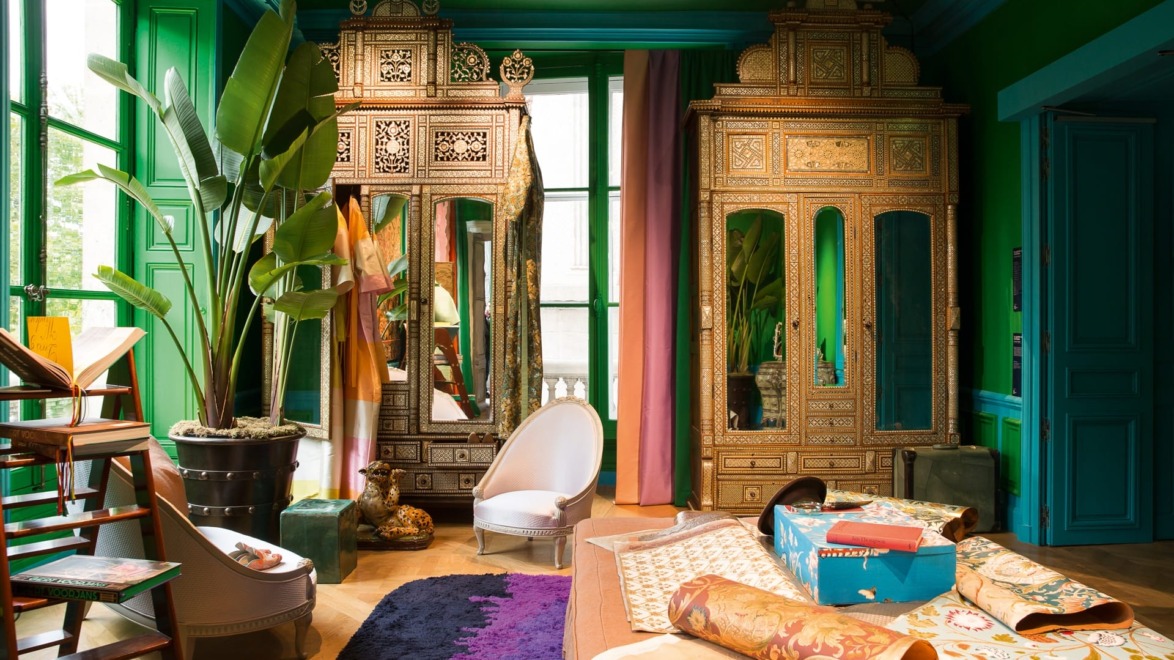 Colorful room with ornate mirrored cabinets, potted plants, and various fabric samples on the floor and chairs.