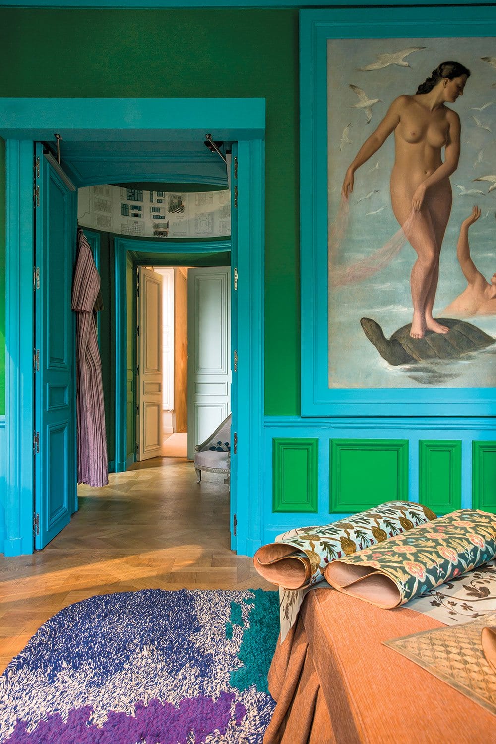 Eclectic room with vibrant green walls, large art piece, colorful rug, and open doorways revealing adjacent rooms.