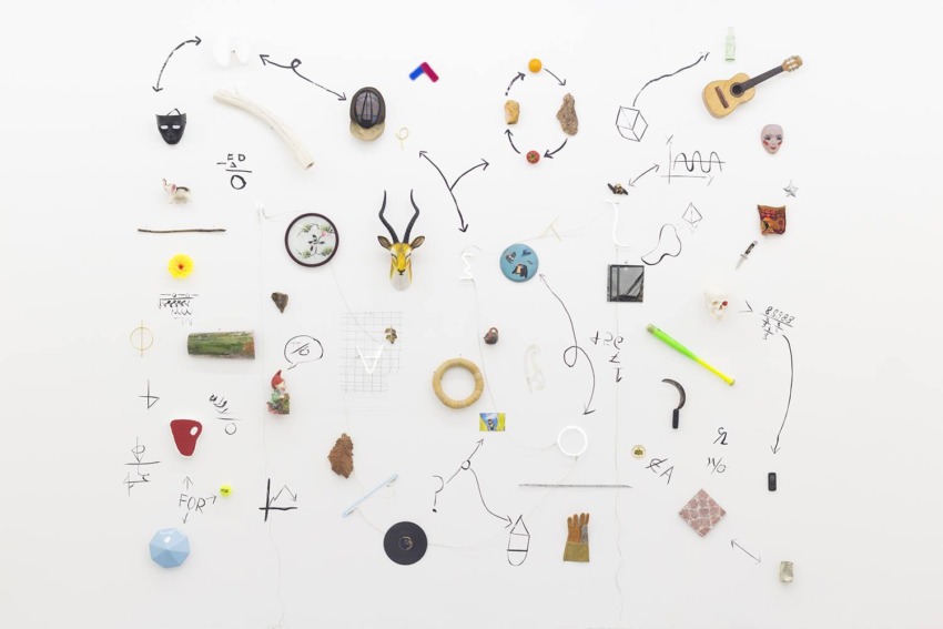 Collection of various small objects and drawings on a white wall arranged in an artistic pattern.