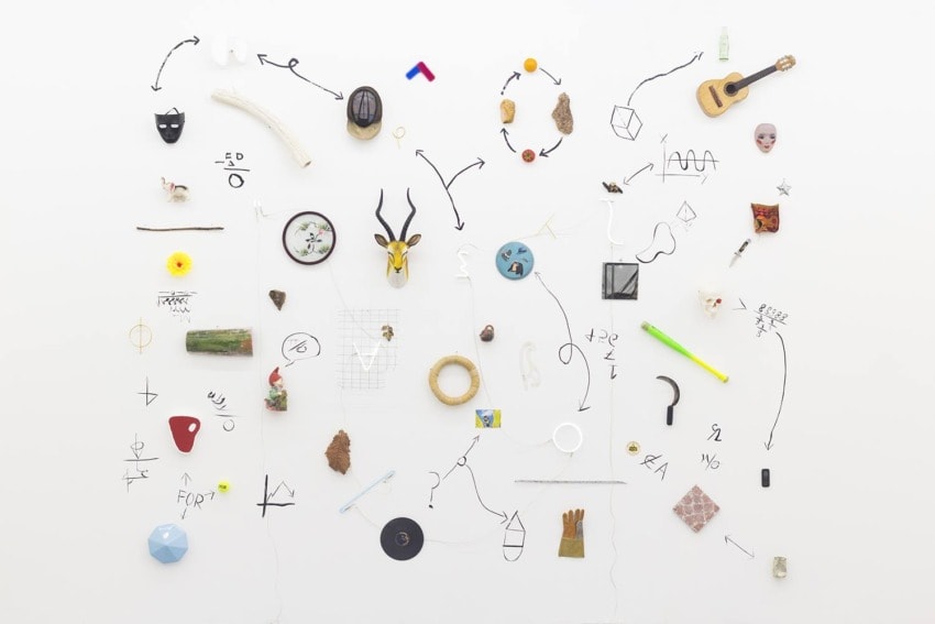 Collection of various small objects and drawings on a white wall arranged in an artistic pattern.
