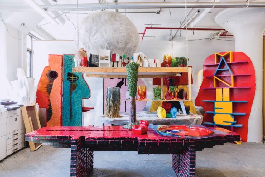 Colorful abstract art installation with vibrant sculptures and geometric shapes arranged on and around a large red table.