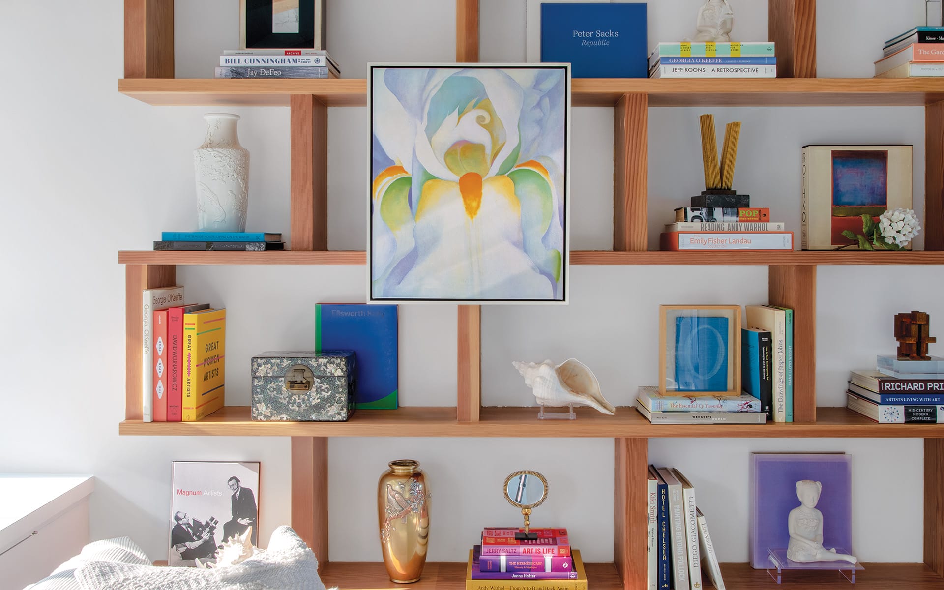 Bookshelf with colorful books, decor, and framed artwork of a flower at the center.