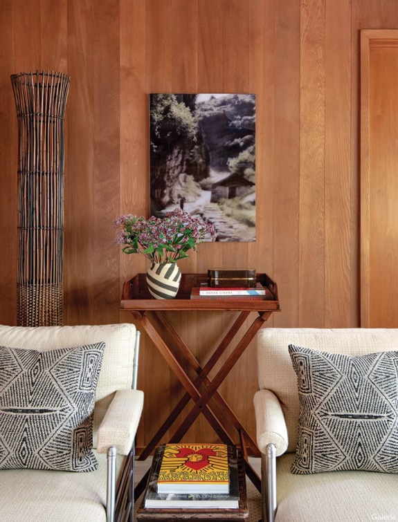 Cozy interior with wooden walls, two armchairs, patterned cushions, a small table, and a decorative vase with flowers.