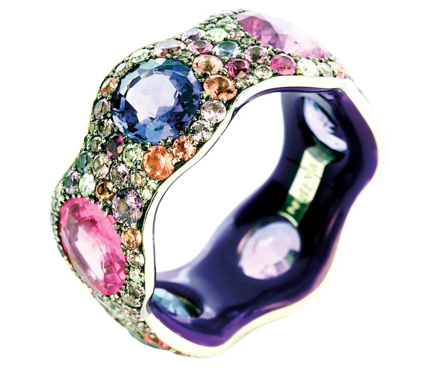 Colorful gemstone encrusted ring with purple, pink, and blue stones on a wave-like silver band, viewed at an angle.