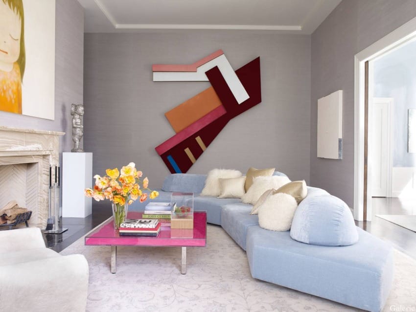 Modern living room with blue sectional sofa, colorful wall art, vibrant flowers on a pink coffee table, and gray walls.