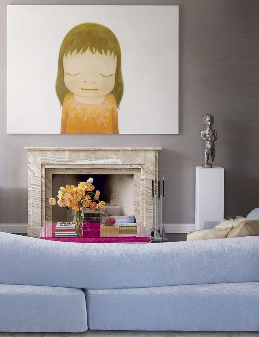 Living room with large artwork above fireplace, light blue sofa, pink coffee table, and a sculpture on a white pedestal.