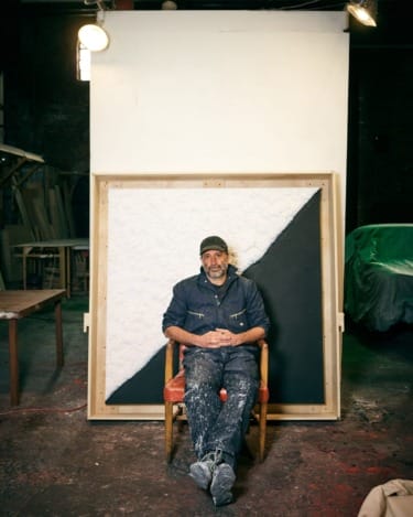 Man sitting on a chair in an art studio, with a monochrome painting in the background.