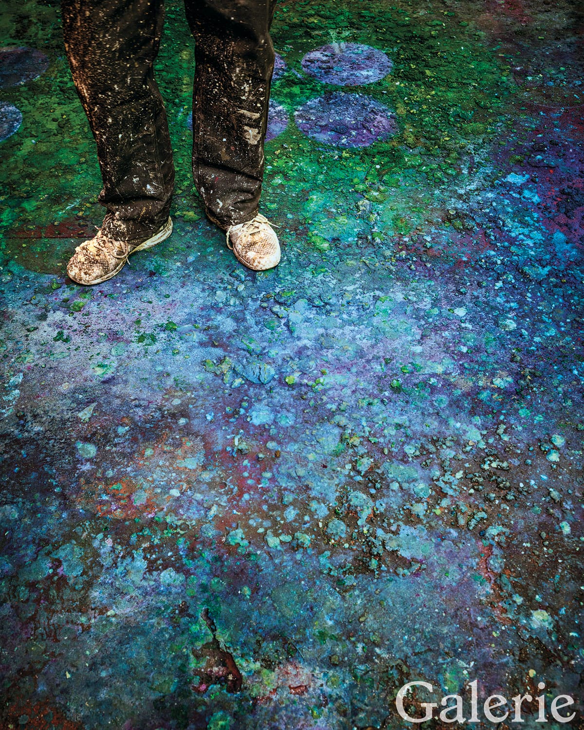 Person standing on colorful, paint-splattered ground, creating an abstract, vivid artistic scene.